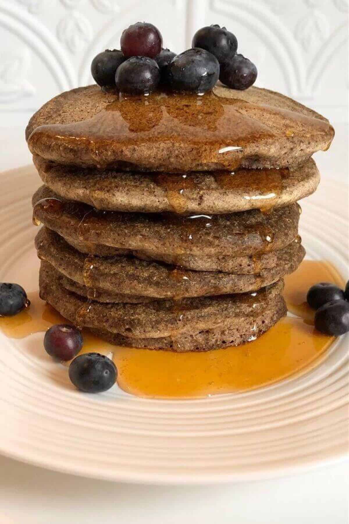 Stack of brown buckwheat pancakes topped with syrup and blueberries on the side. 