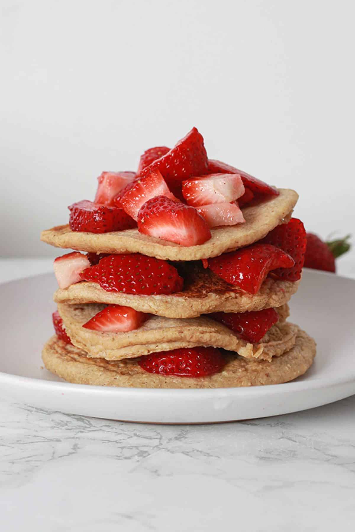 Four pancakes stacked and sliced strawberries in between them. 