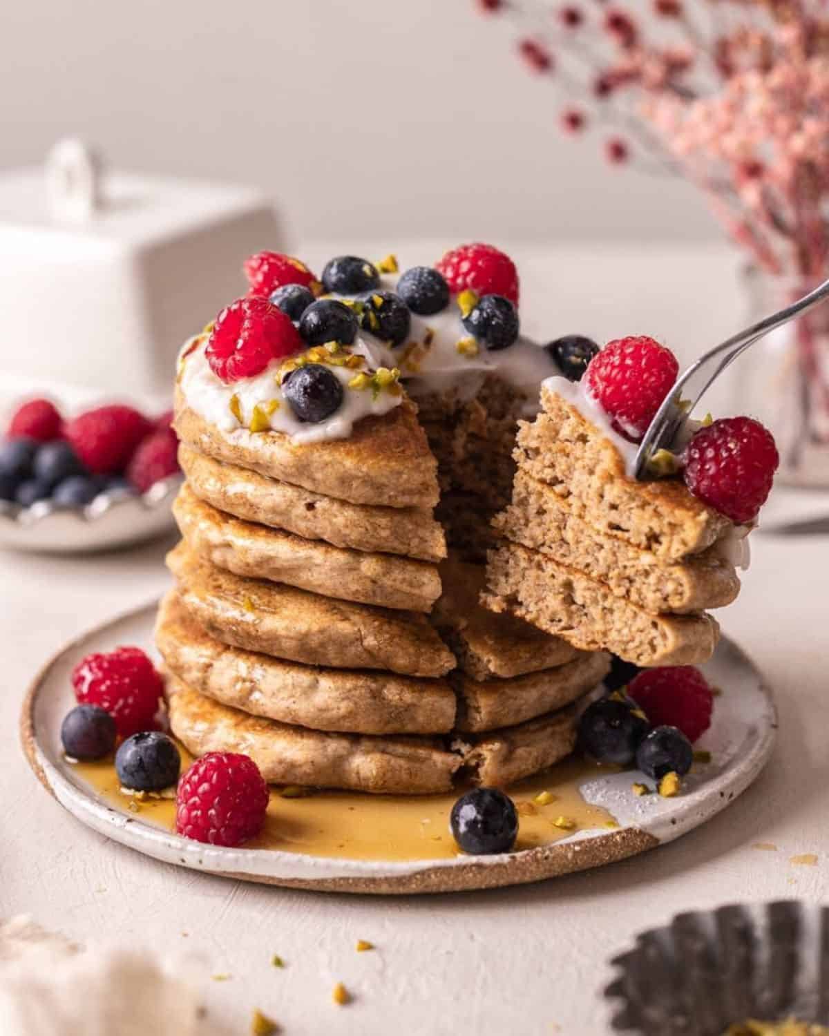 Stack of pancakes topped with cream, syrup, blueberries and raspberries. The stack is cut into quarters. 
