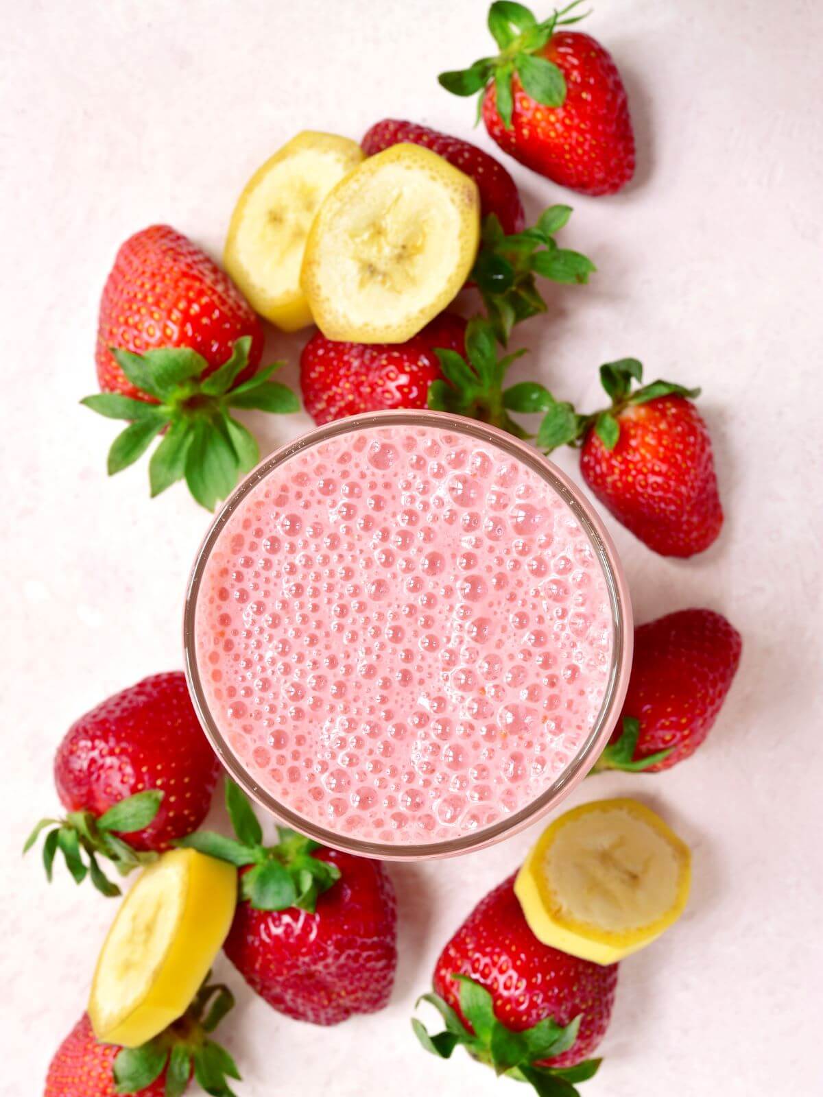 Pink smoothie with strawberries and bananas on the side. 