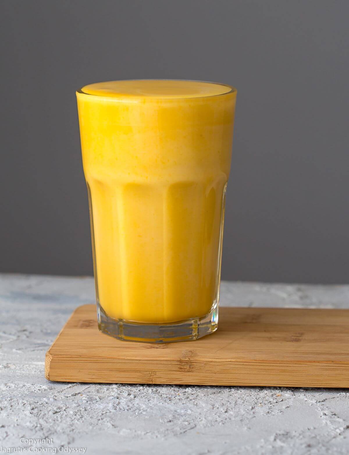 Glass with a yellow smoothie on a wooden table. 