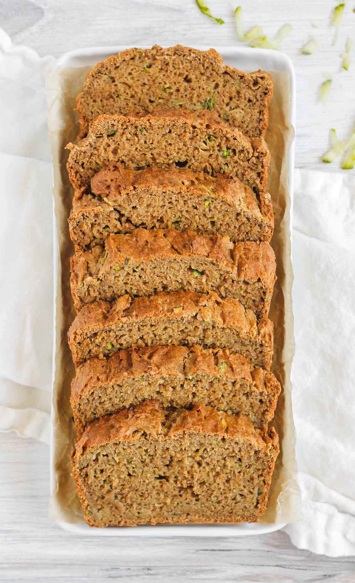 Slices of zucchini bread lined up in a white baking tin. 