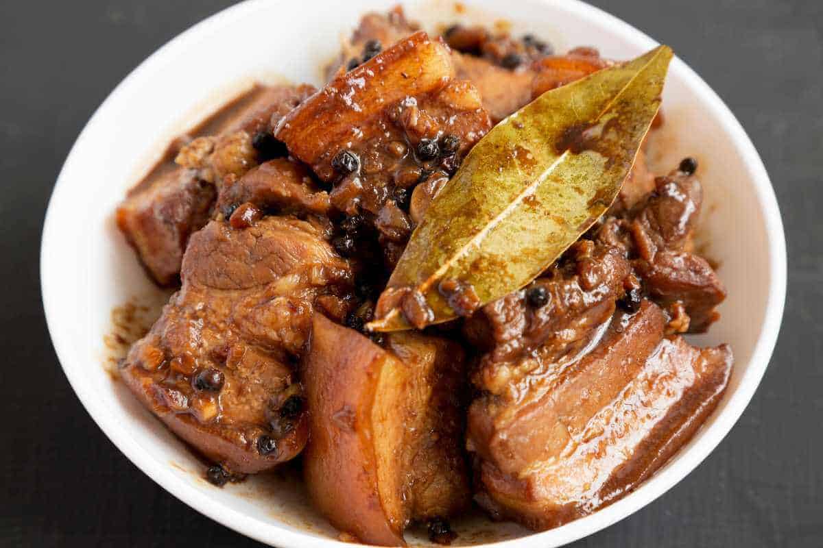 A bowl of meat prepared with adobo and with a bay leaf on top