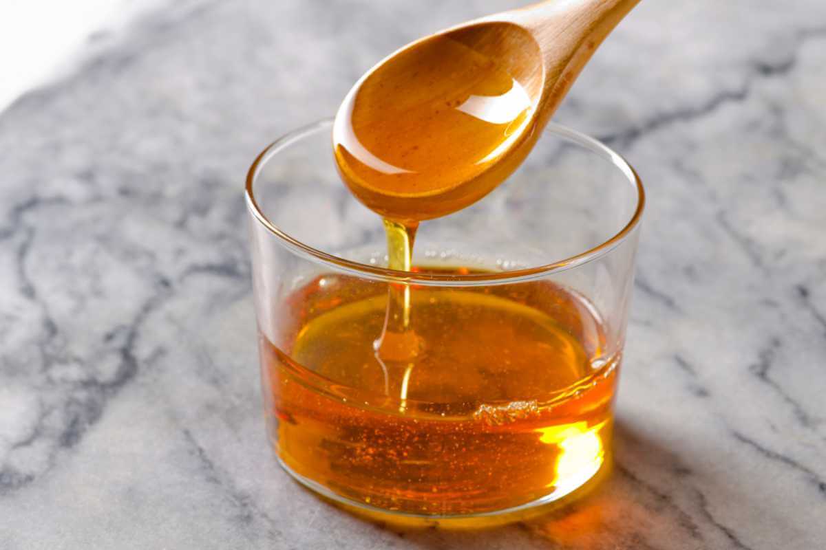 A cup of agave syrup with a wooden spoon dripping with syrup