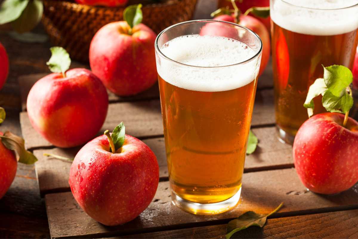 A glass of ale on a table next to some apples