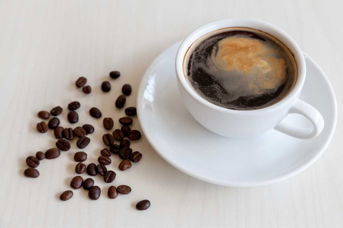 A cup of coffee (americano) on a table next to some coffee beans