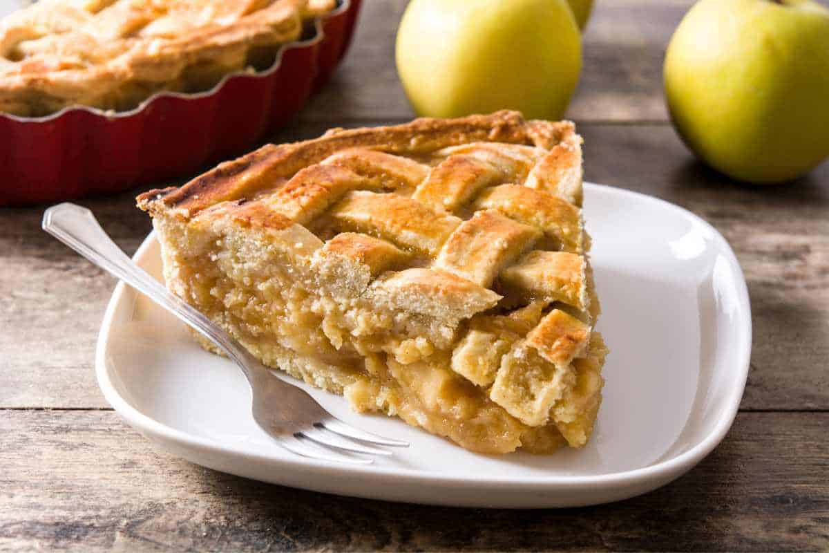 A wedge of apple pie on a plate with a fork