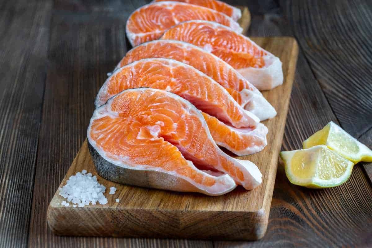 Some arctic char steaks on a board with some salt and lemon