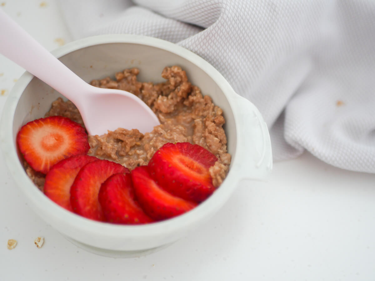 landscape image of the oatmeal with cut up strawberries and a spoon dipped in 