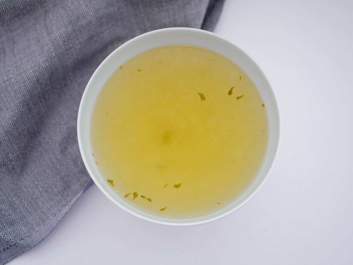 clear chicken soup in a white bowl with small bits of parsley floating 