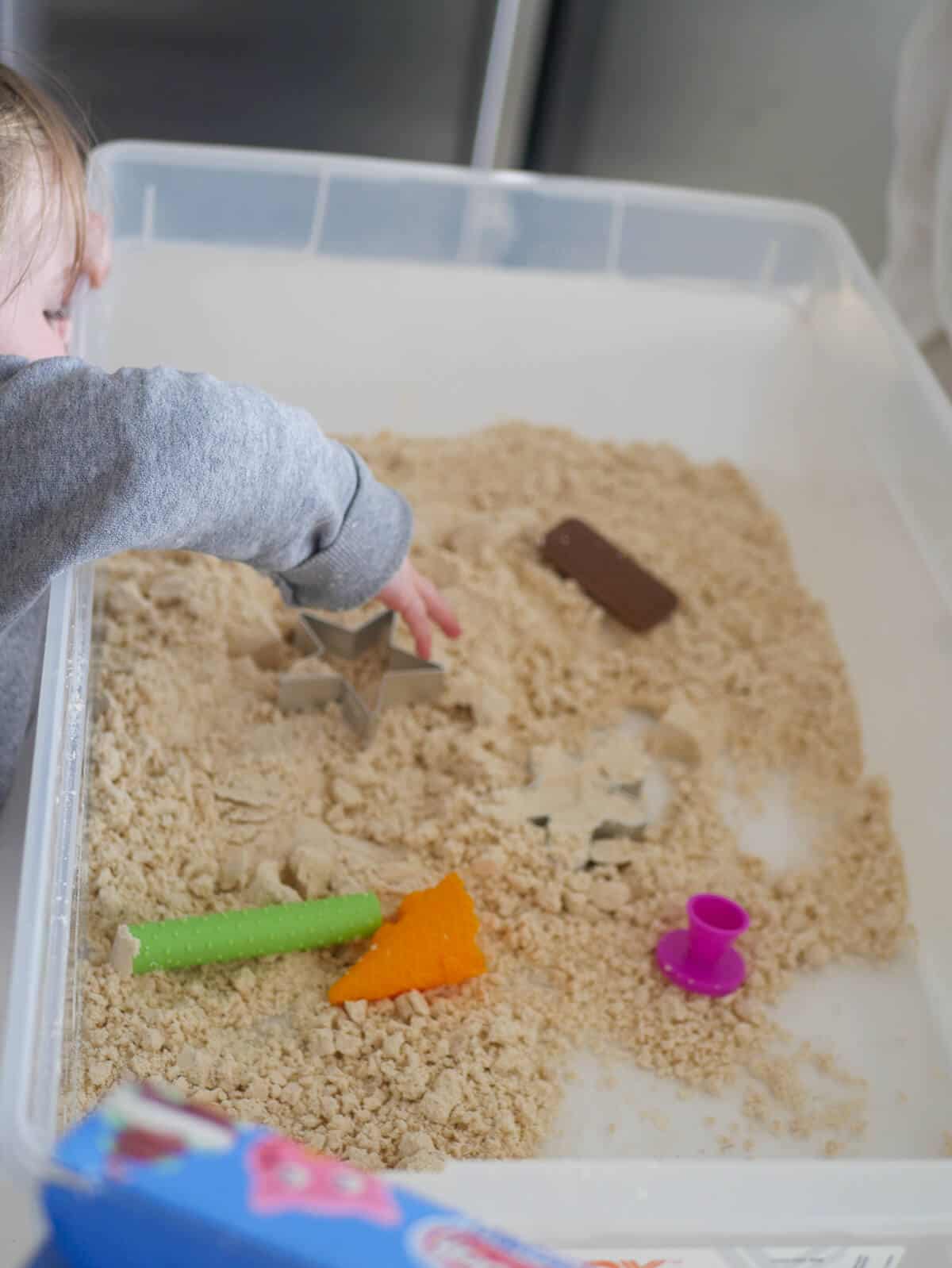 child playing with moon sand an playdough toys in sensory bin 