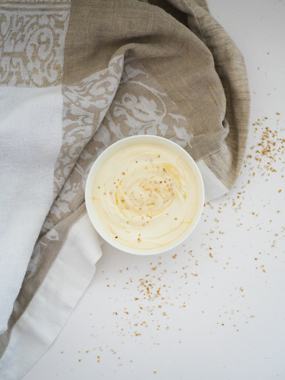 birds eye view of vanilla yogurt in a bowl with small oats sprinkled on and around 