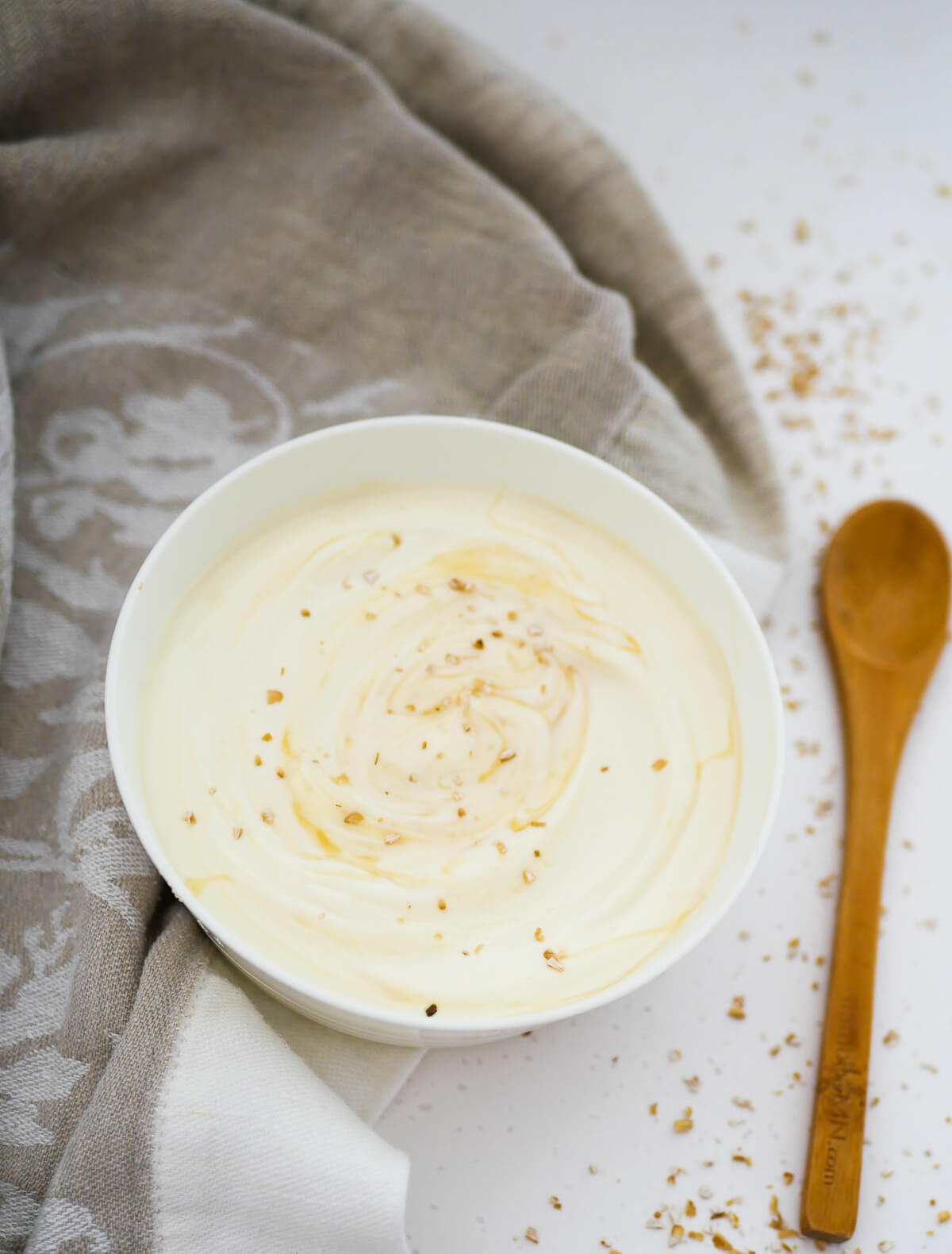 vanilla yogurt in a white bowl with a brownish cloth and wooden spoon in background 