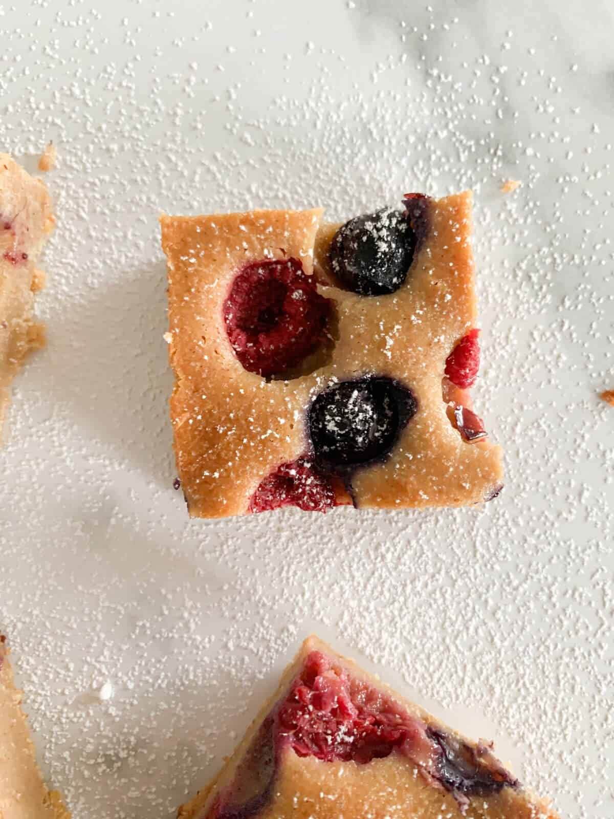 One piece of yogurt fruit cake sprinkled with caster sugar. Raspberries and blueberries in the yogurt fruit cake piece.