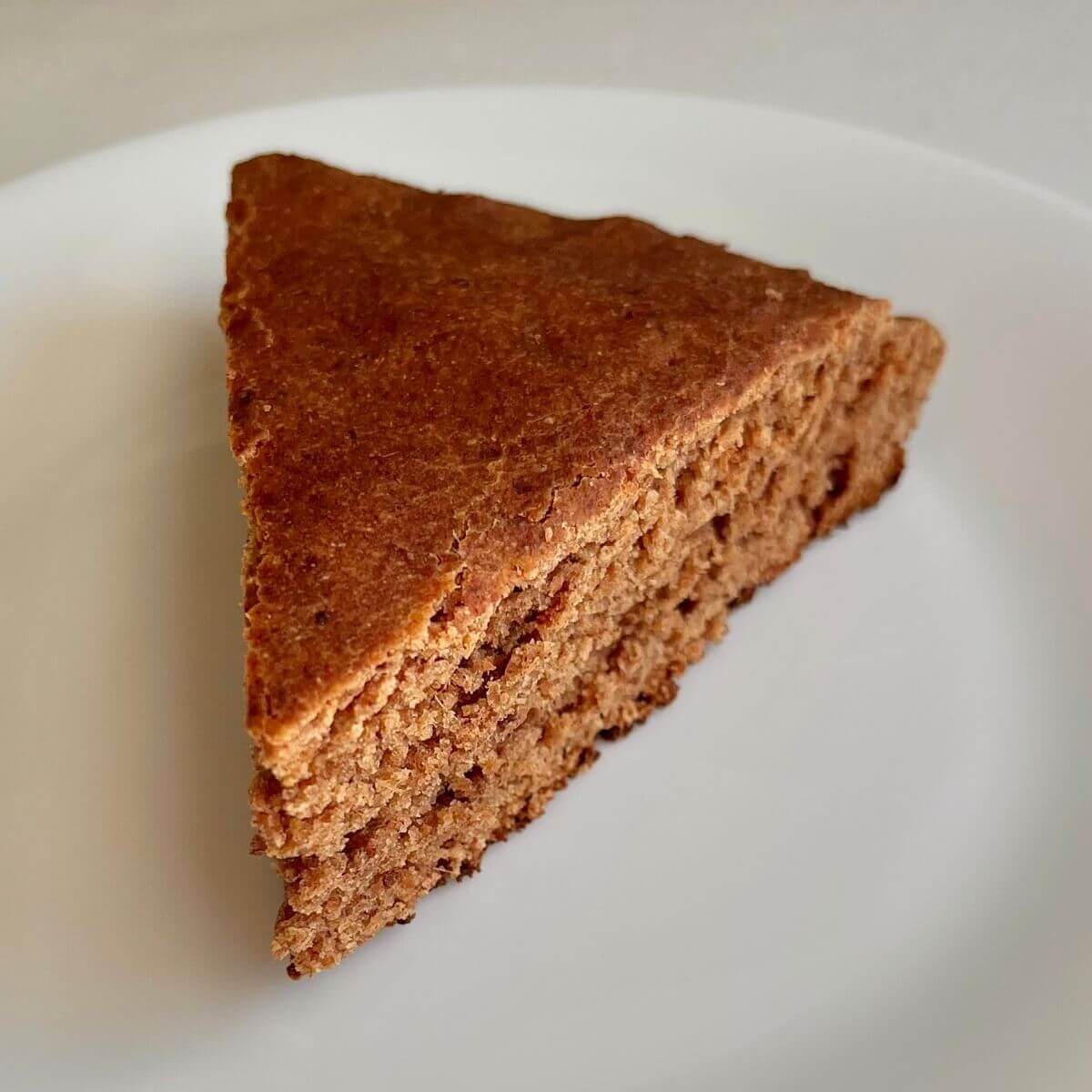 Spelt cake cut in a triangle piece on a white plate.