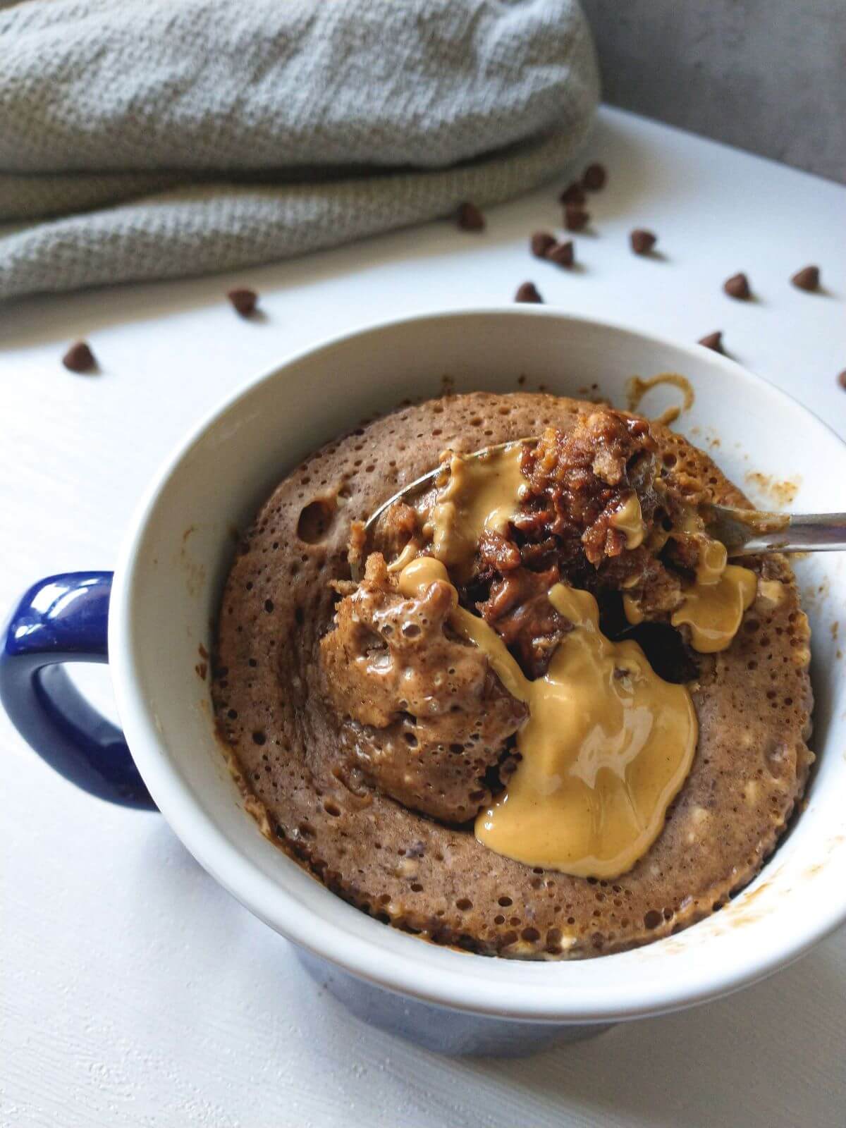 Mug cake with spoon and peanut butter in a blue and white mug. 