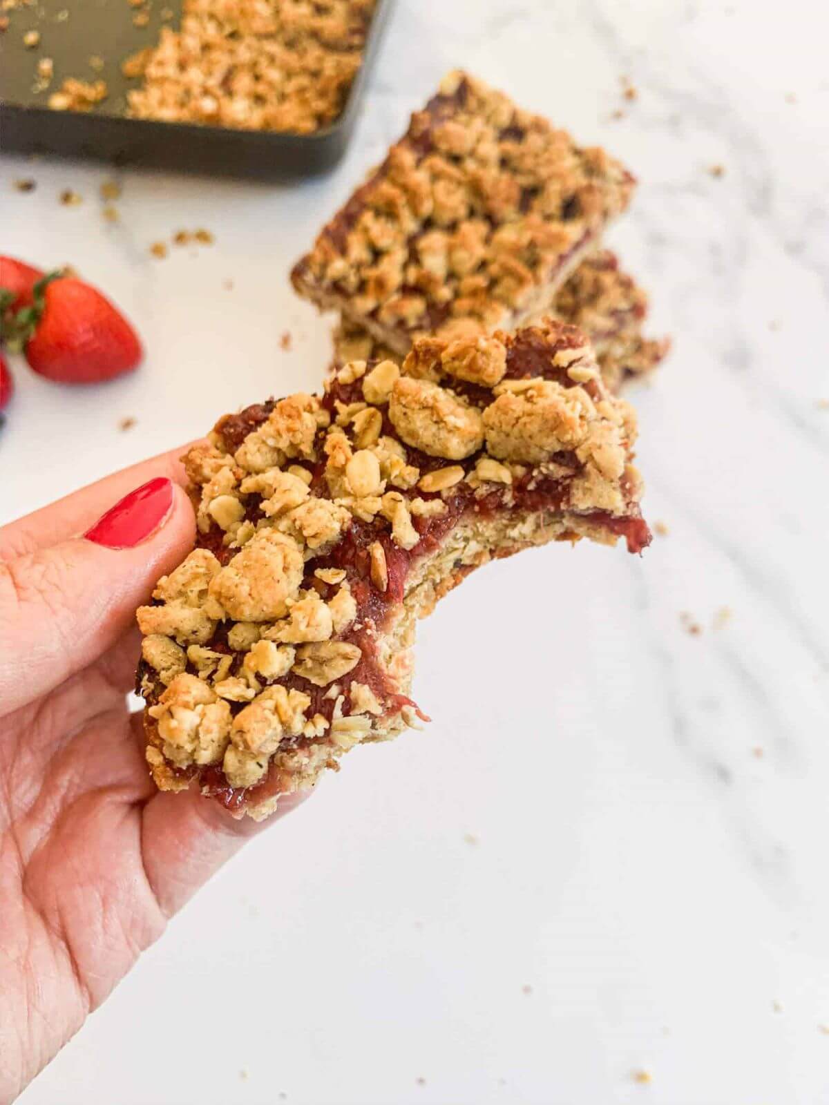 A hand holding a strawberry oatmeal bar where somebody has already taken a bite. 