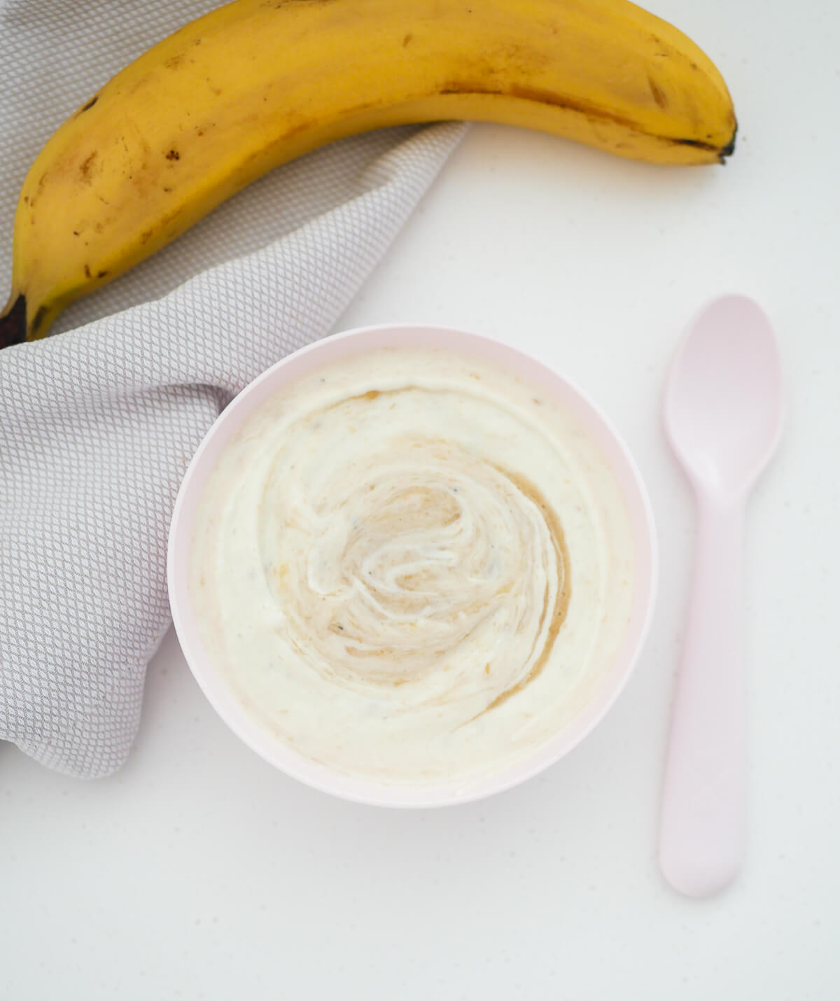 portrait image of banana yogurt in a pink bowl with a spoon next to it 