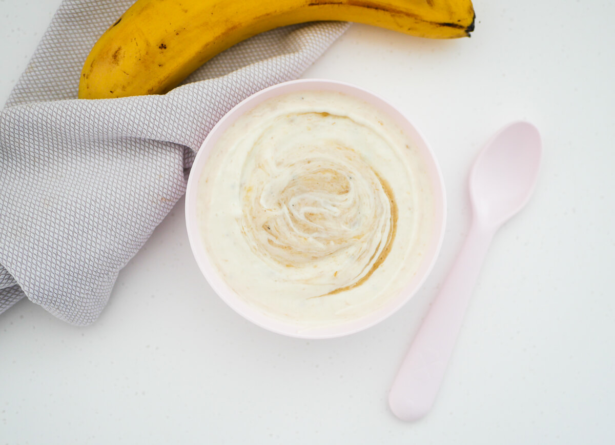 landscape image of banana yogurt in a pink bowl with a spoon next to it