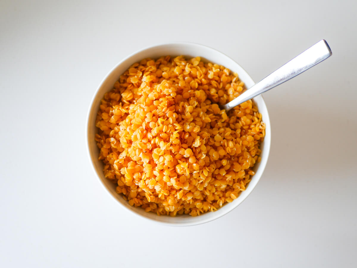 cooked red lentils in white bowl with a silver spoon dipped in