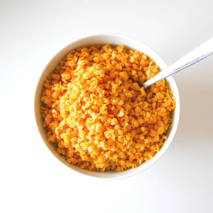 cooked red lentils in white bowl with a silver spoon dipped in