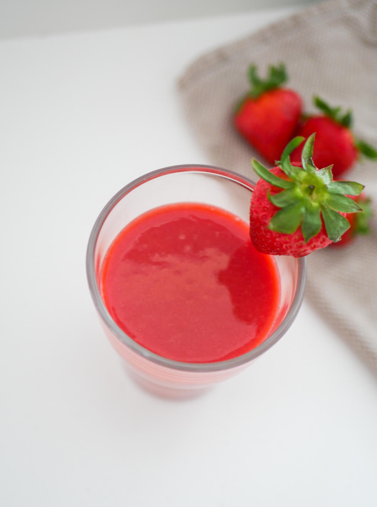 partial birdsye view of strawberry juice in a glass and a strawberry on top of the glass 