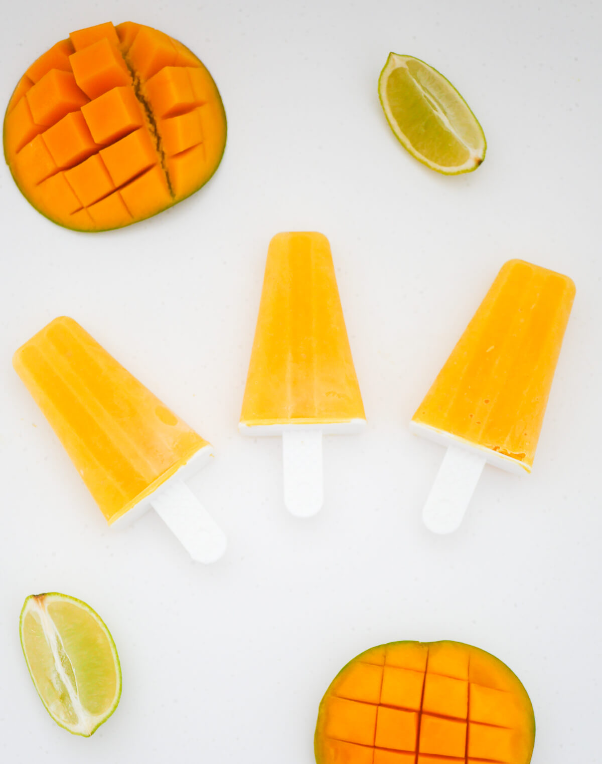 3 orange popsicles on white background with fresh mango and lime in background