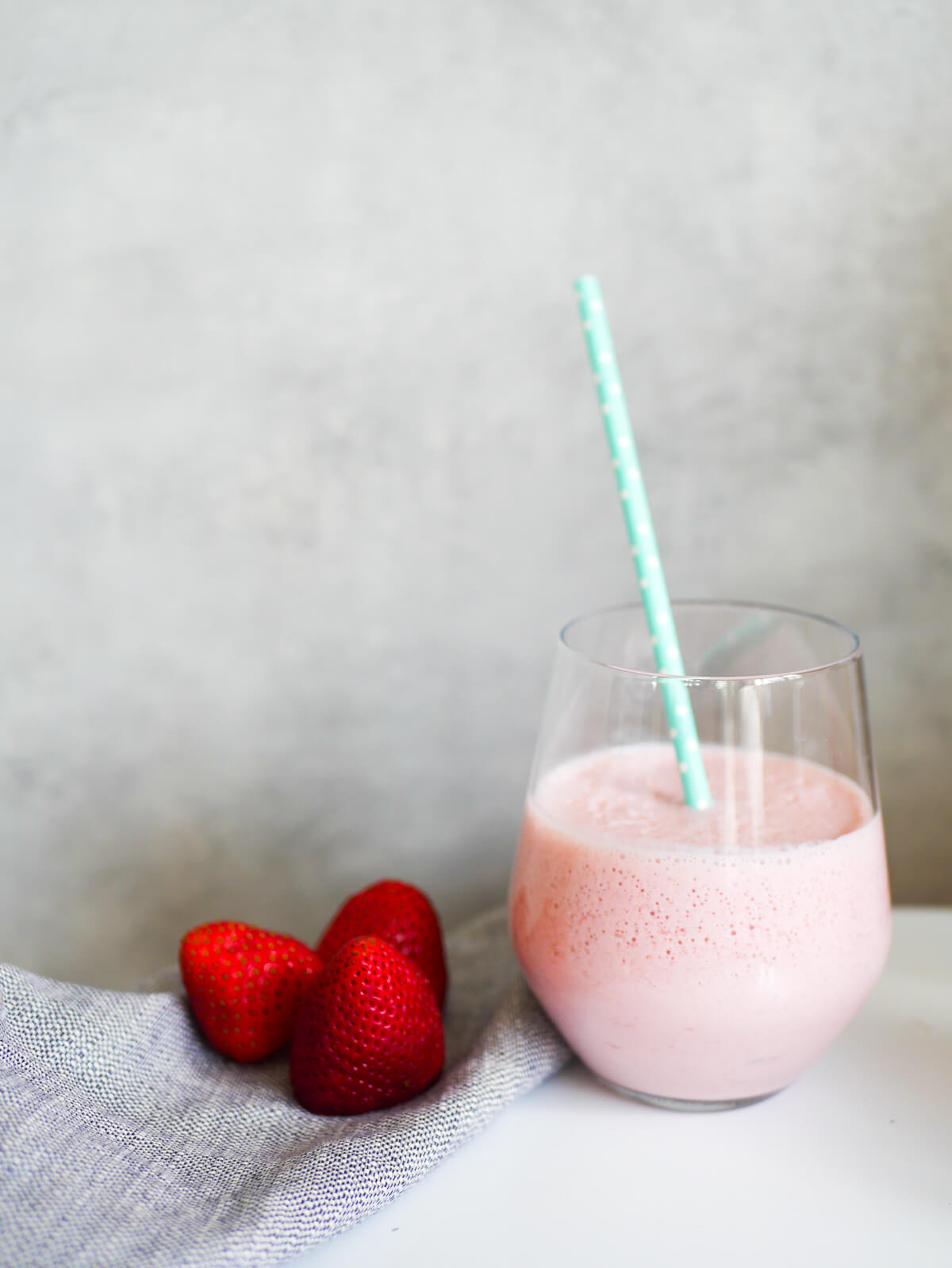 strawberry milk in a glass with grey background and a couple of strawberries beside it