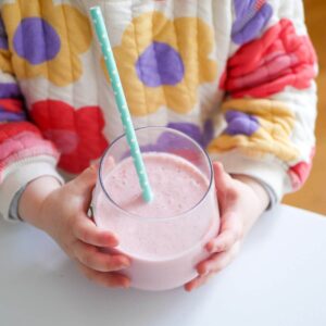 toddler holding glass with strawberry milk