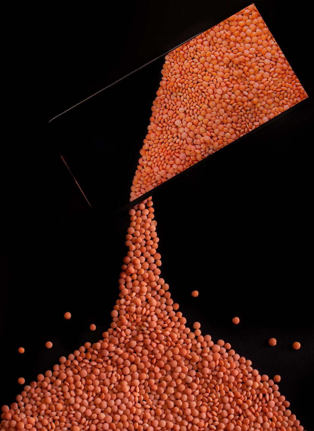 red lentils being poured to a black background from a seethrough glass jar
