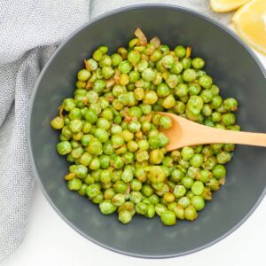 cooked peas in a black bowl with a wooden spoon