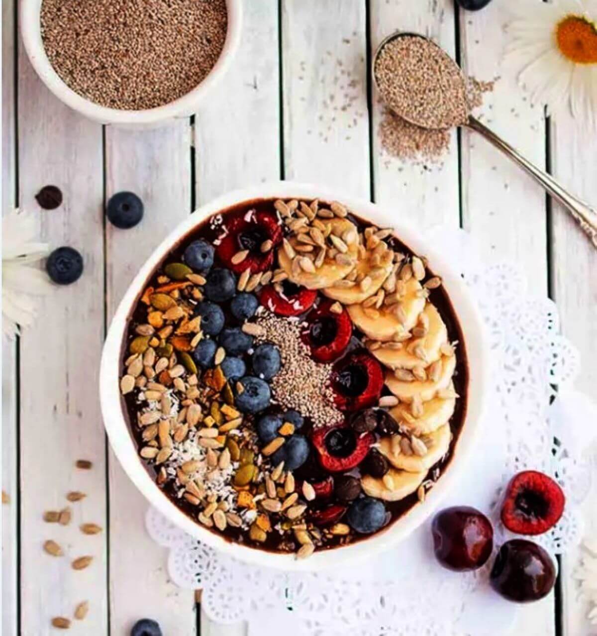 Bowl with a smoothie topped with bananas, raspberries, blueberries, nuts and seeds. 