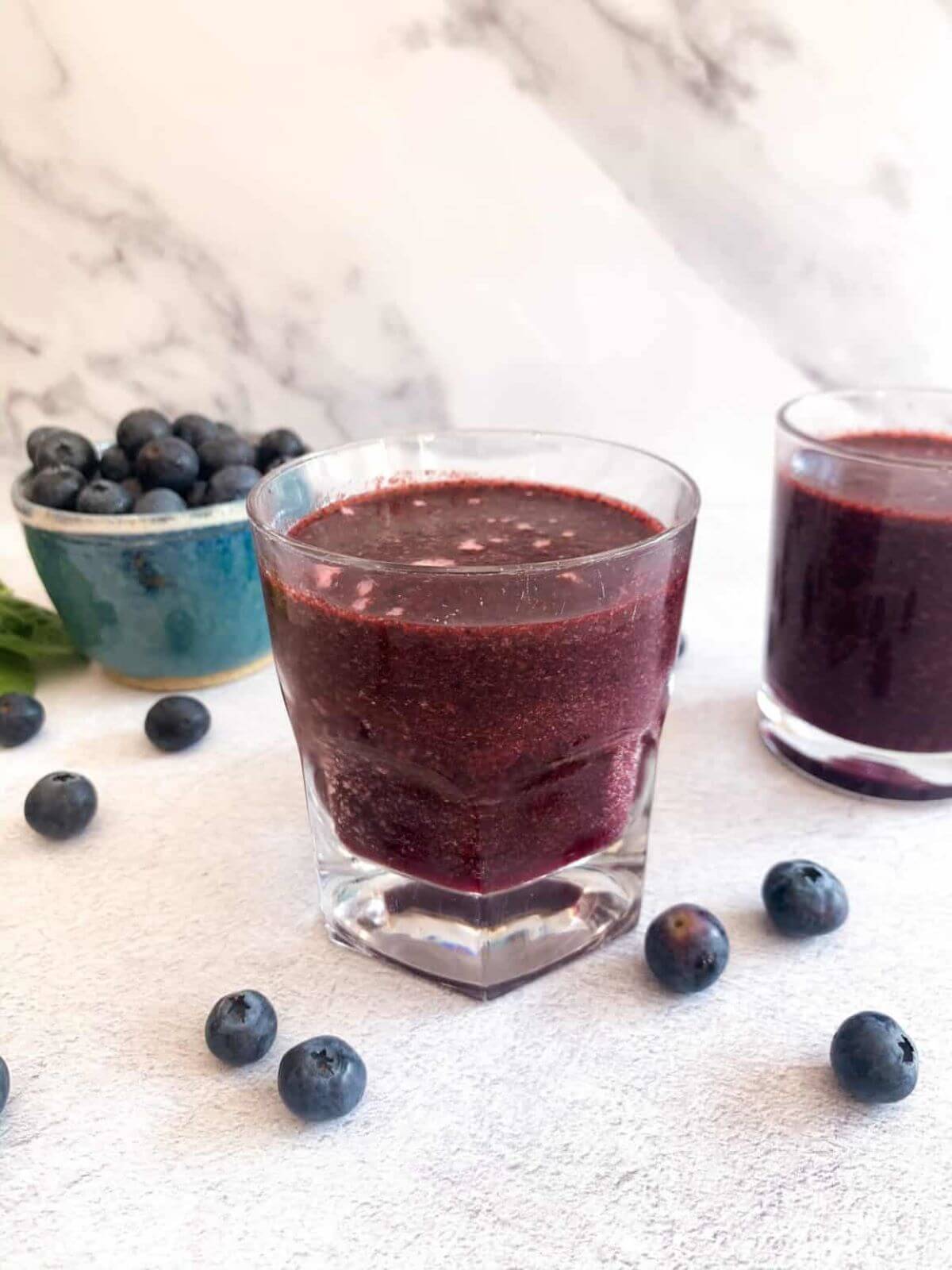 A glas with a purple smoothie and some blueberries on the side. 