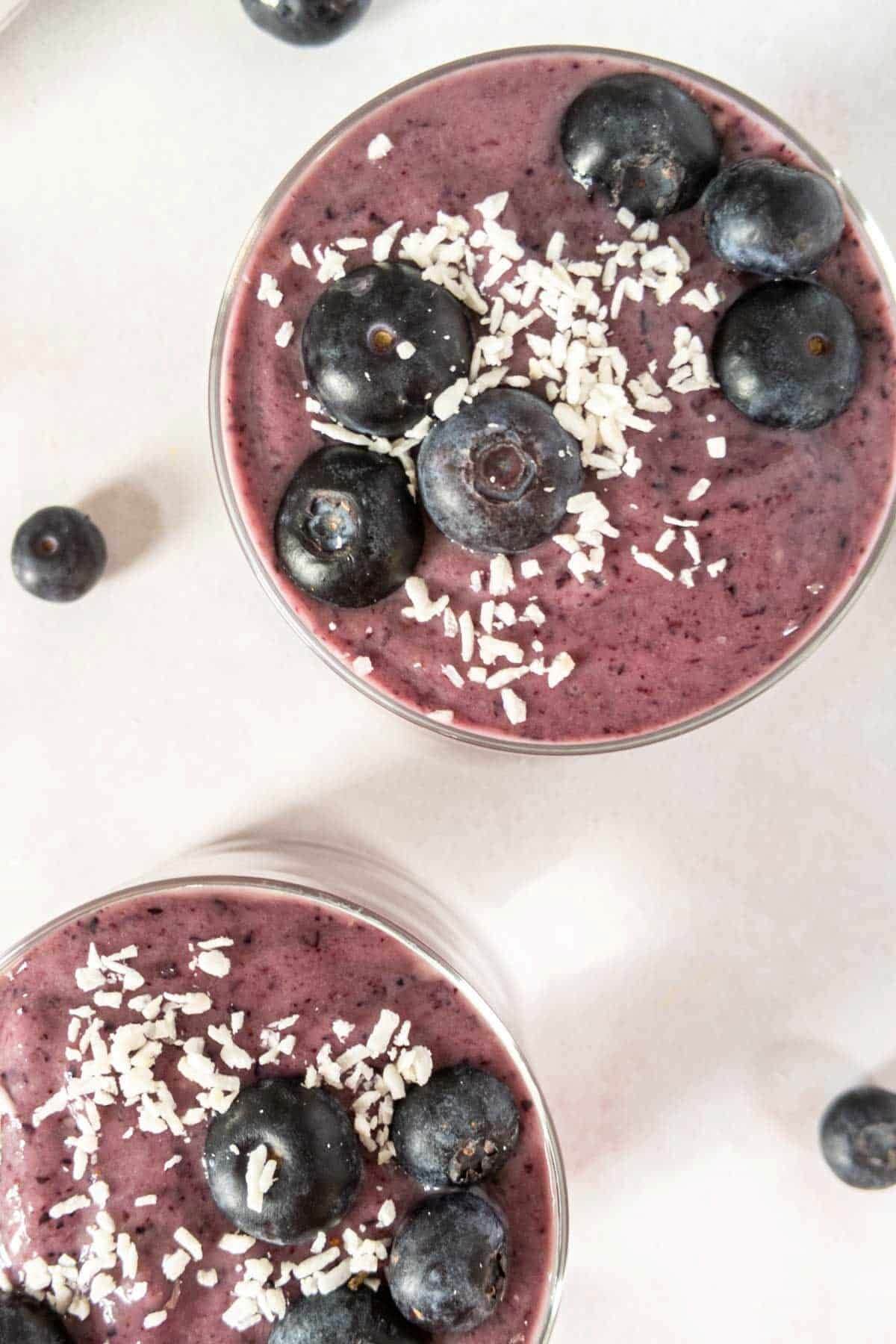 Two smoothie bowls with a purple smoothie topped with shredded coconut and blueberries. 