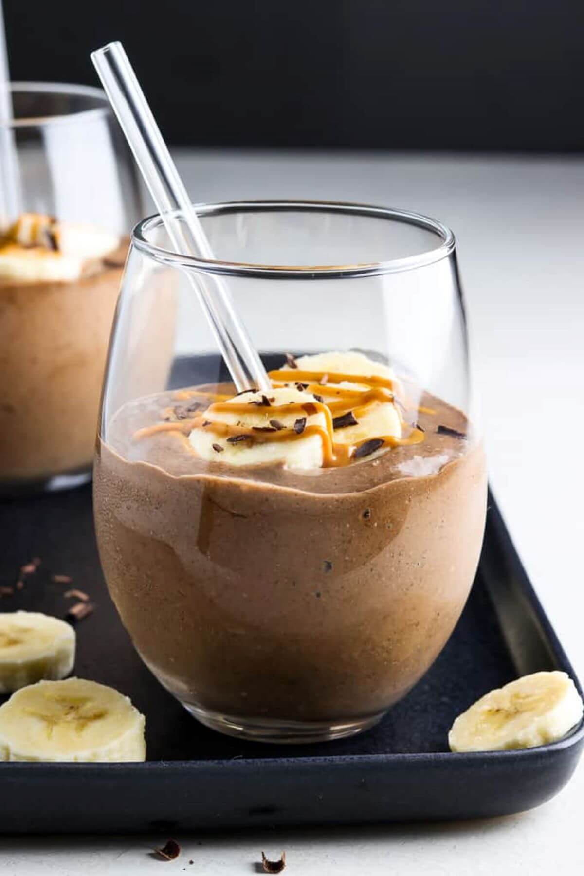 Glas with a brown chocolate smoothie topped with sliced bananas and nut butter. 