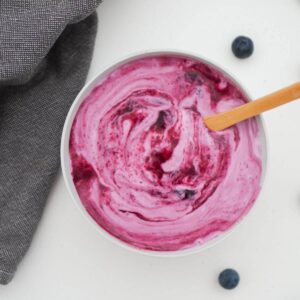 Homemade Blueberry yogurt in a grey bowl with a wooden spoon dipped in