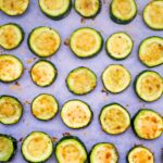 close up of roasted zucchini slices with parmesan cheese on parchment paper
