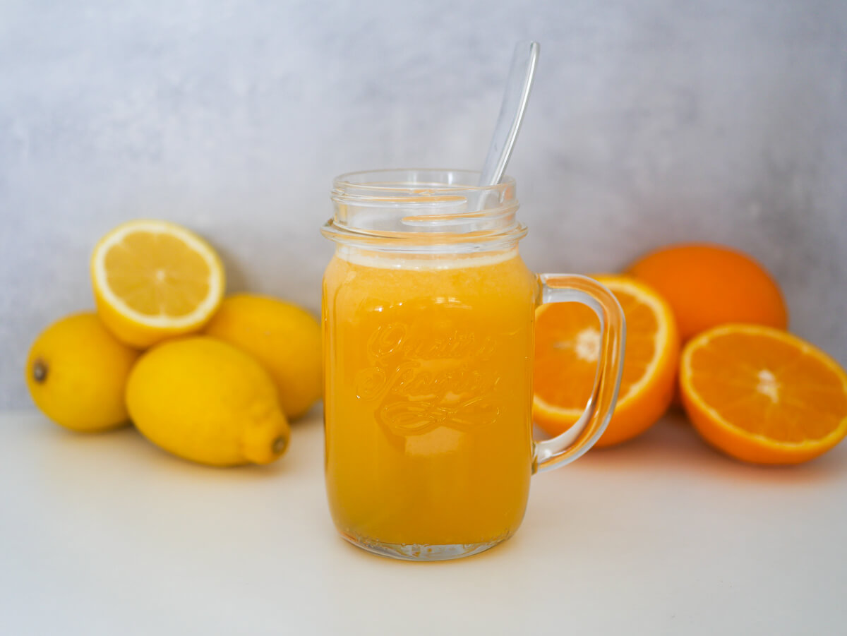 homemade electrolyte drink in a glass with cut up oranges and lemons in the background