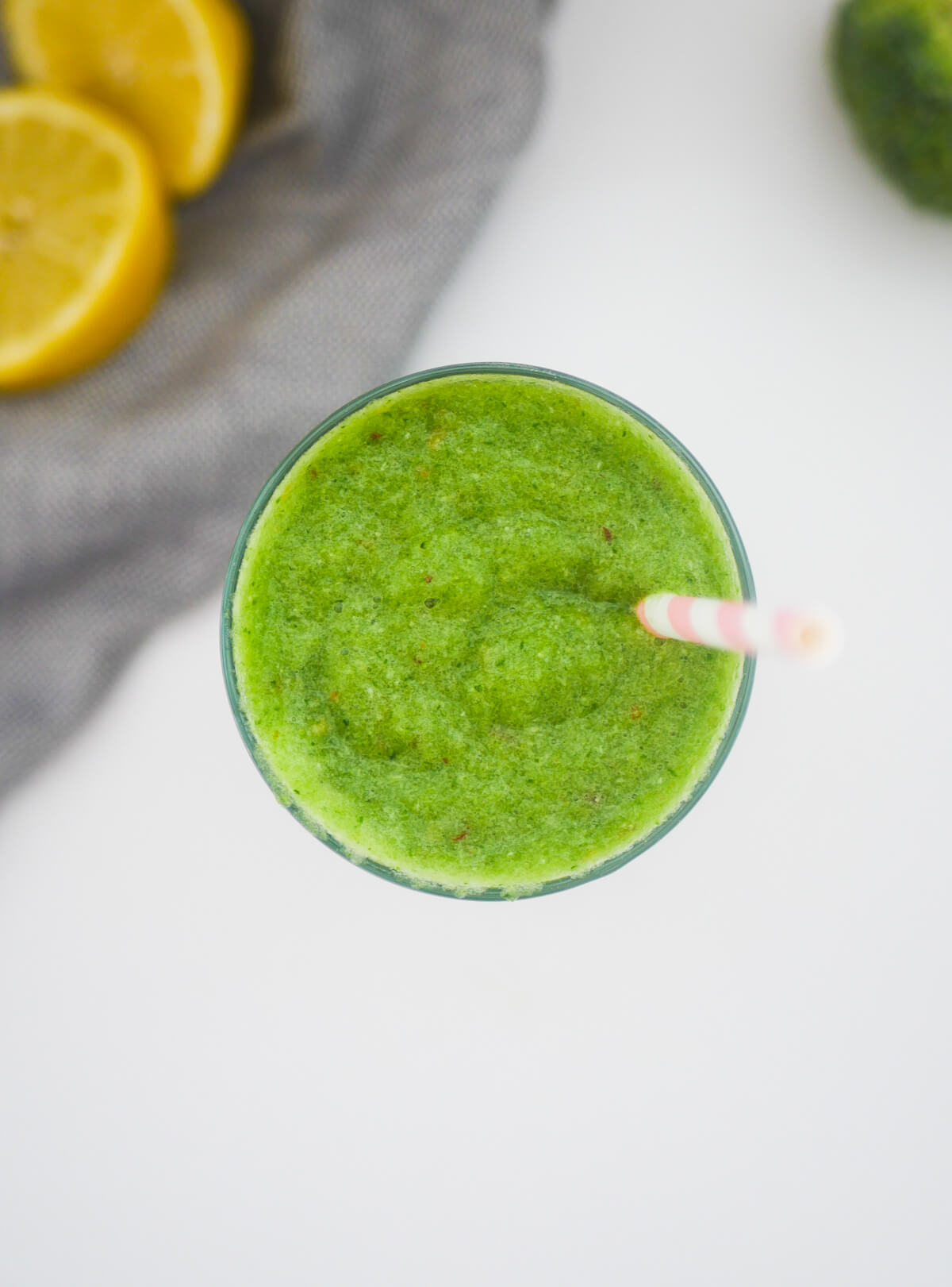 top down image of bright green broccoli smoothie with lemons in background