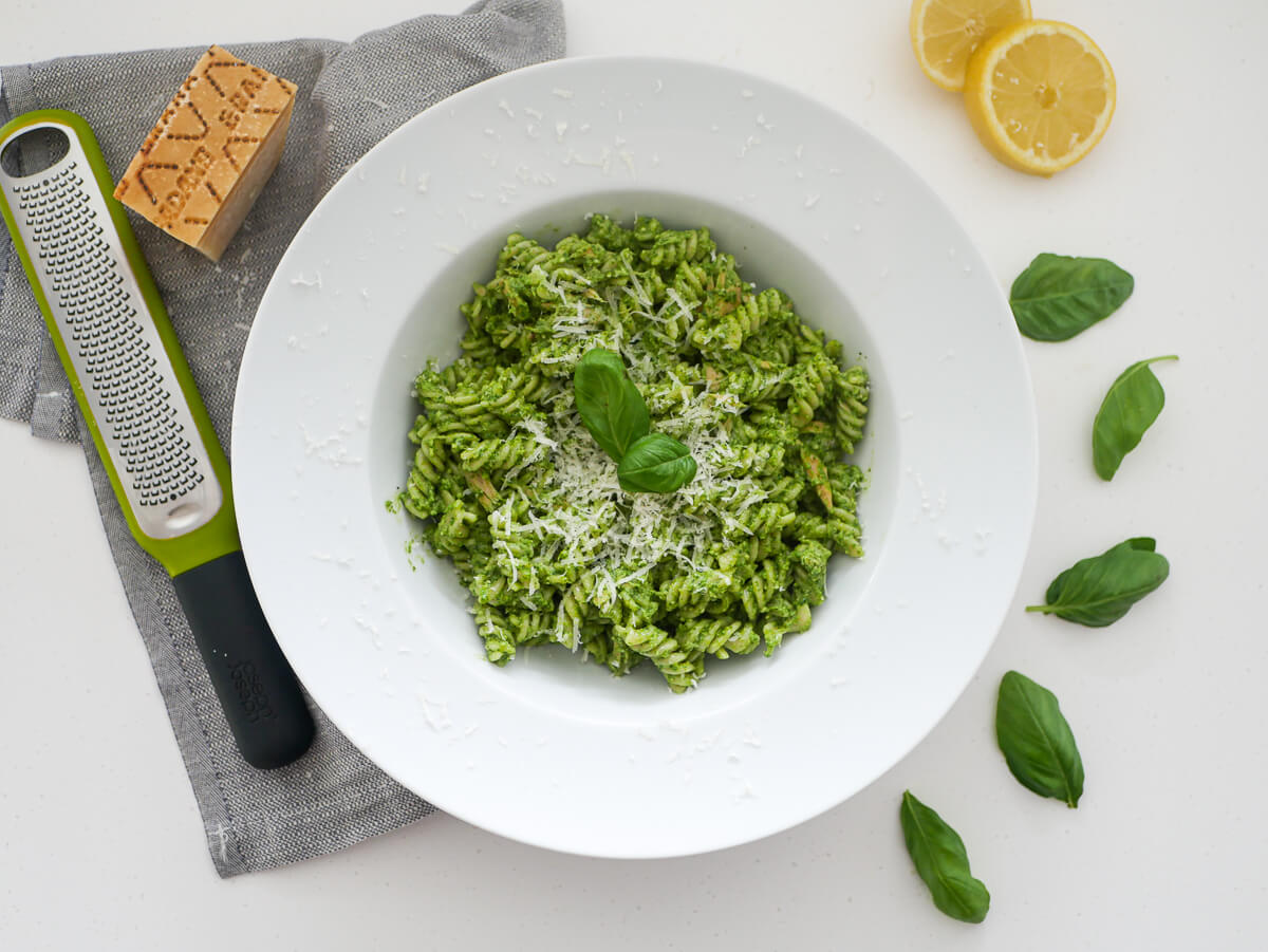 tuna pesto pasta in a white bowl with lemons, basil leaves and grater in the background