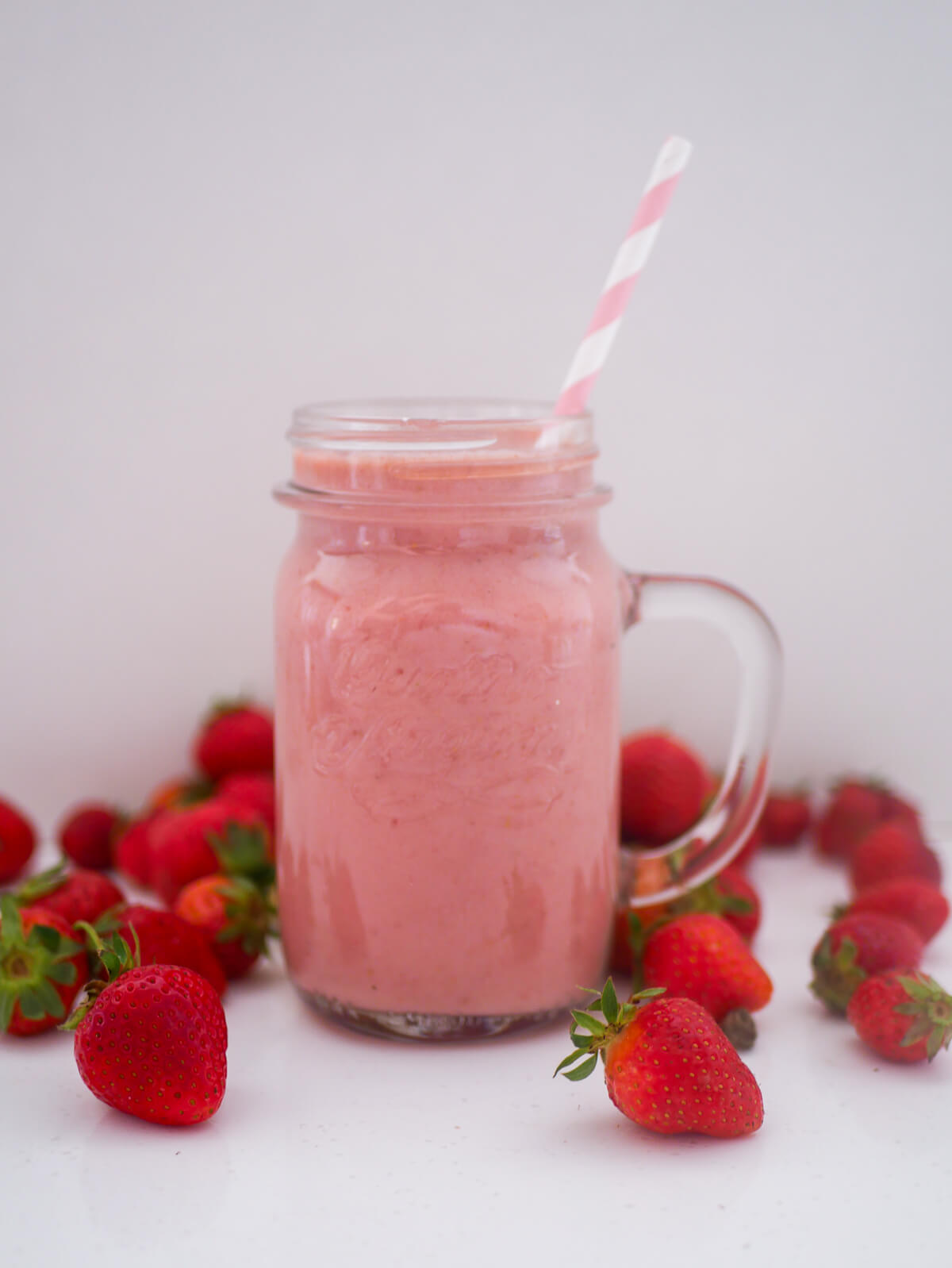 pink milkshake in a glass with strawberries in the background