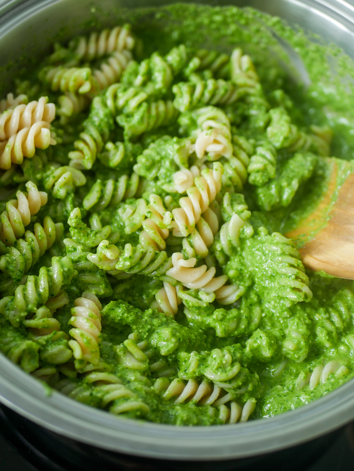 white fusilli in a suacepan mixed with a green pasta sauce