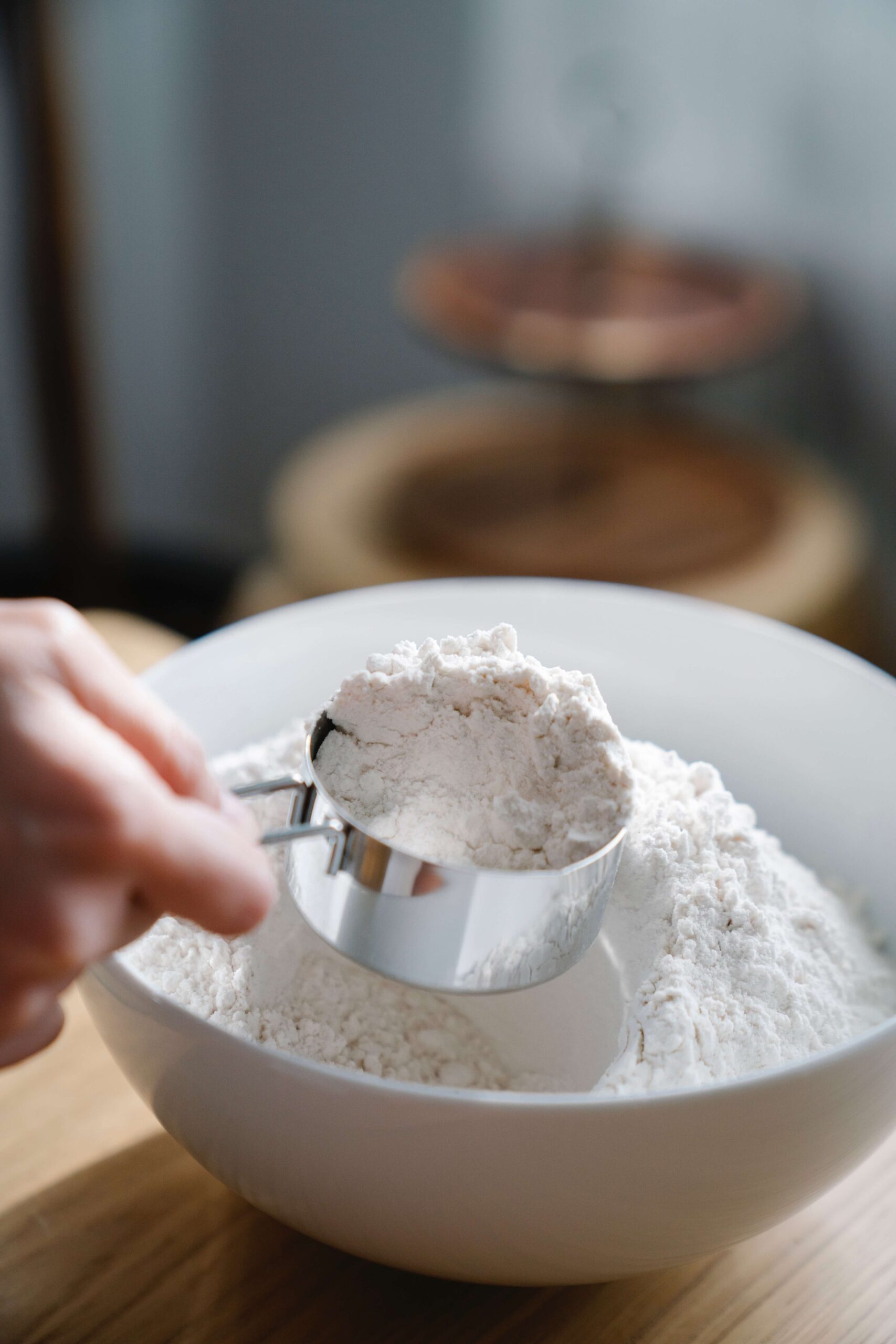 A measuring cup being used to scoop flour out of a bowl