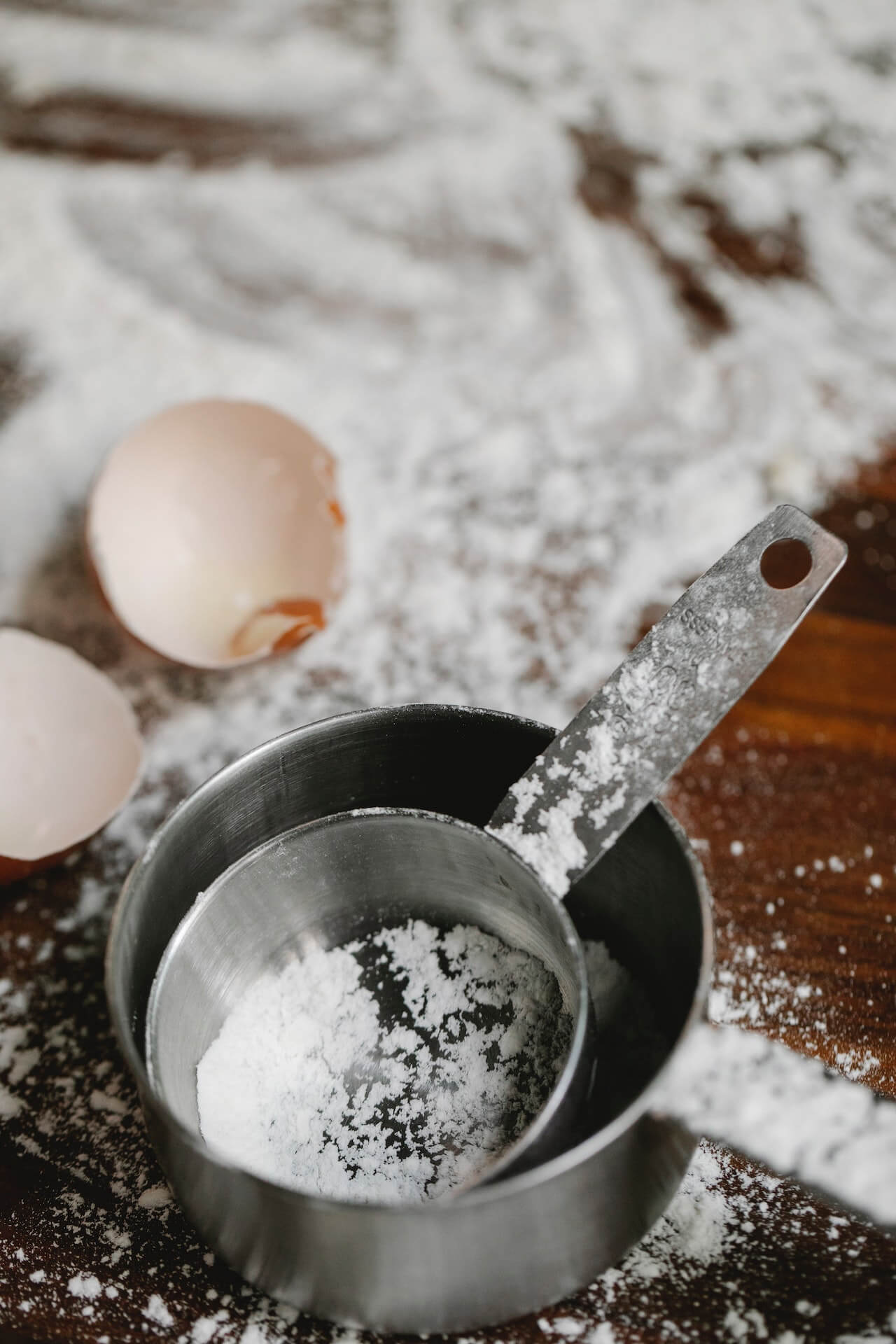 1 cup and a ¼ cup on a table with some flour on them and egg shells in the background