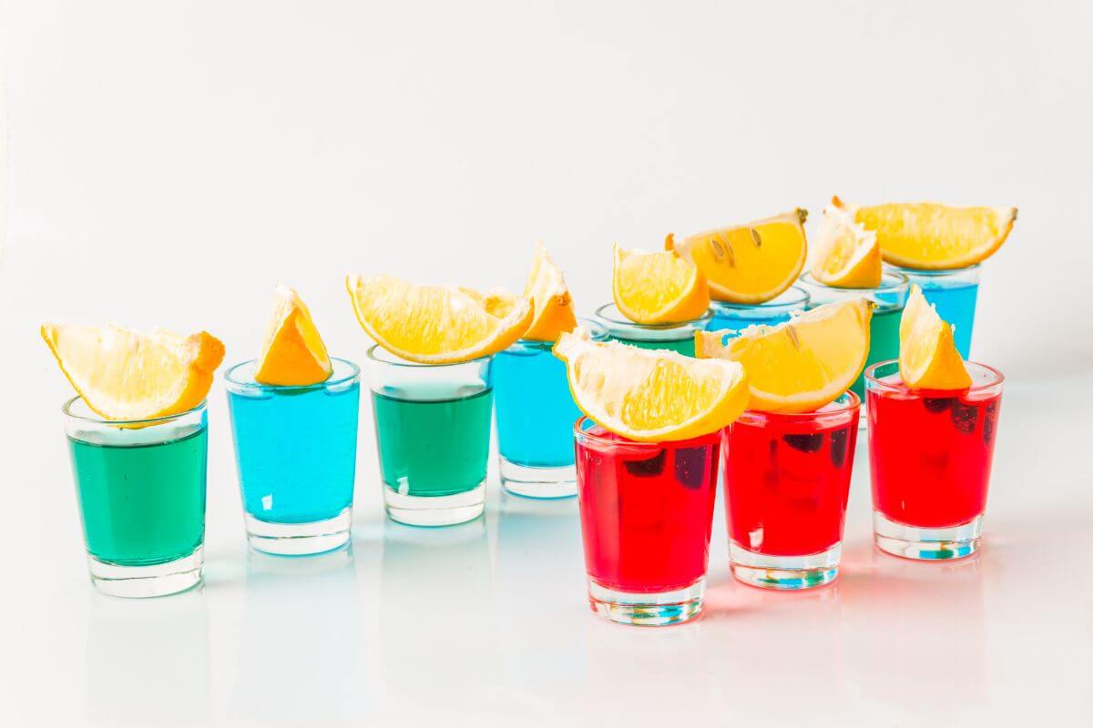 A line of 8 blue and green kamikaze shots, behind 3 red kamikaze shots, each with a lemon slice balanced on top