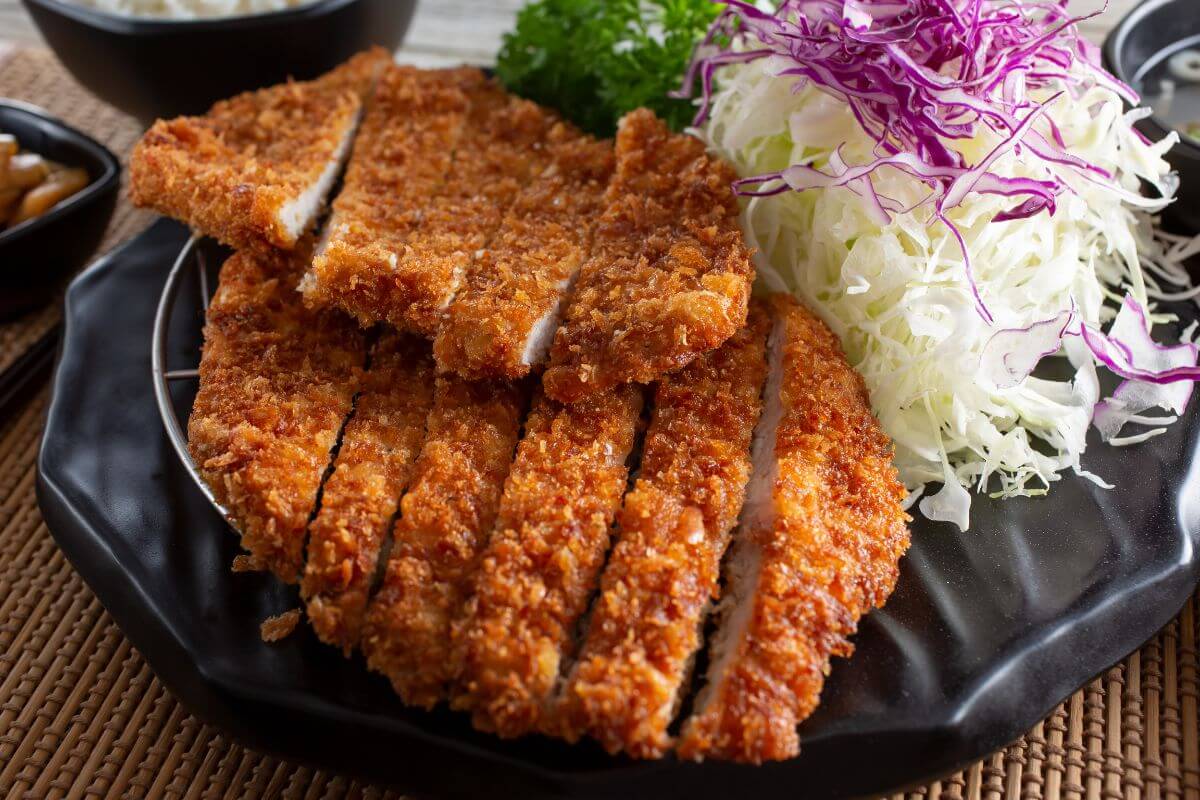 A plate of sliced katsu chicken next to a cabbage salad