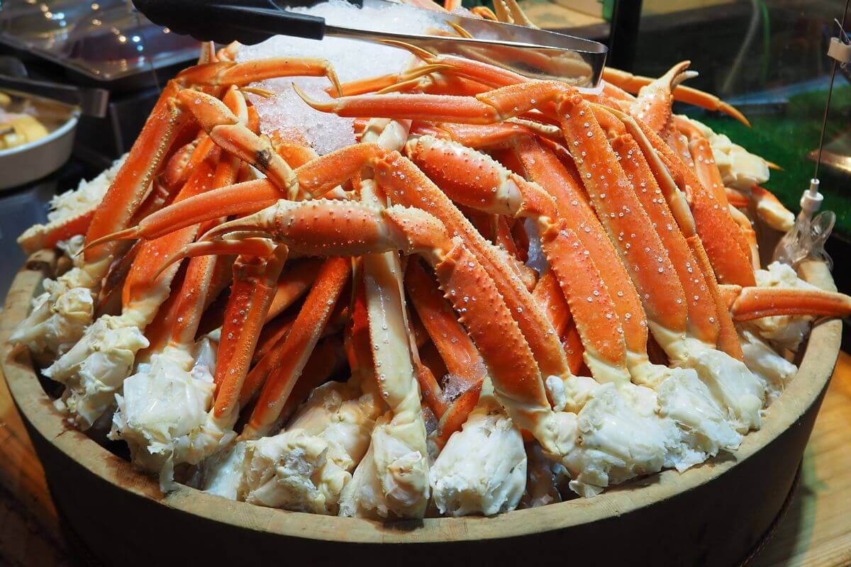 A pile of king crab legs, surrounded by white crab meat in a big wooden bowl