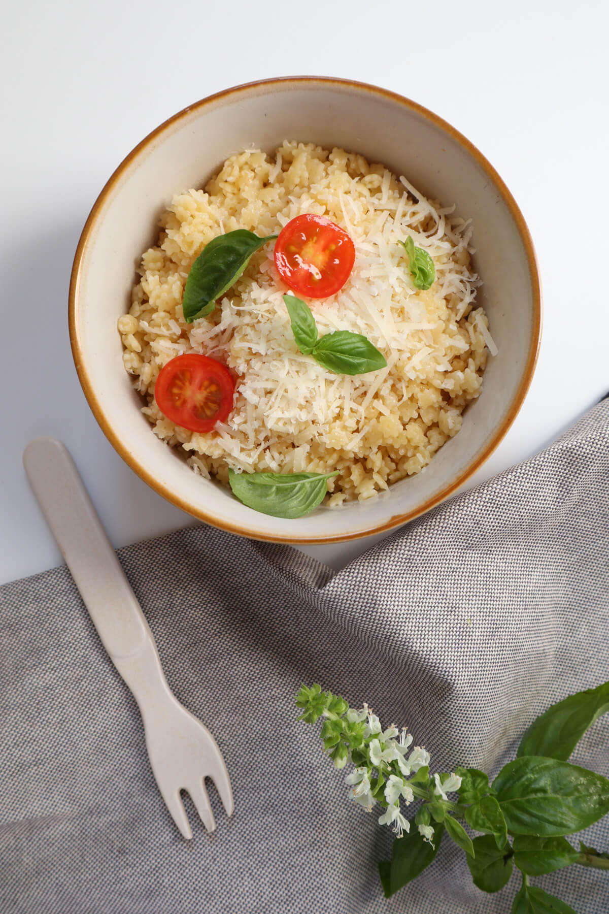 Pastina in a bowl topped with cherry tomatoes and basil leaves and a fork and grey tablecloth on the side.