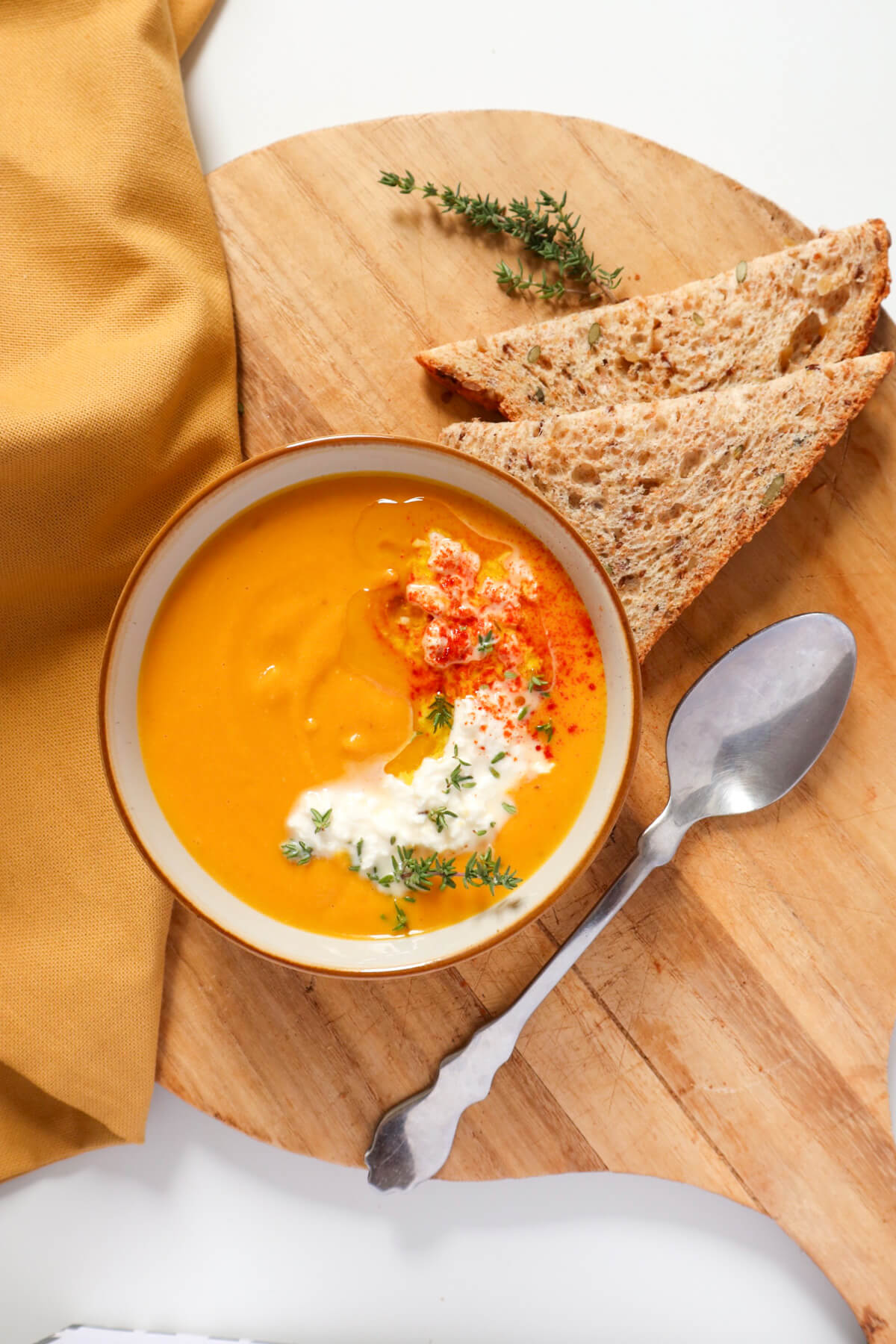 carrot and red lentil soup in a bowl topped with olive oil and feta and bread and a spoon next to it