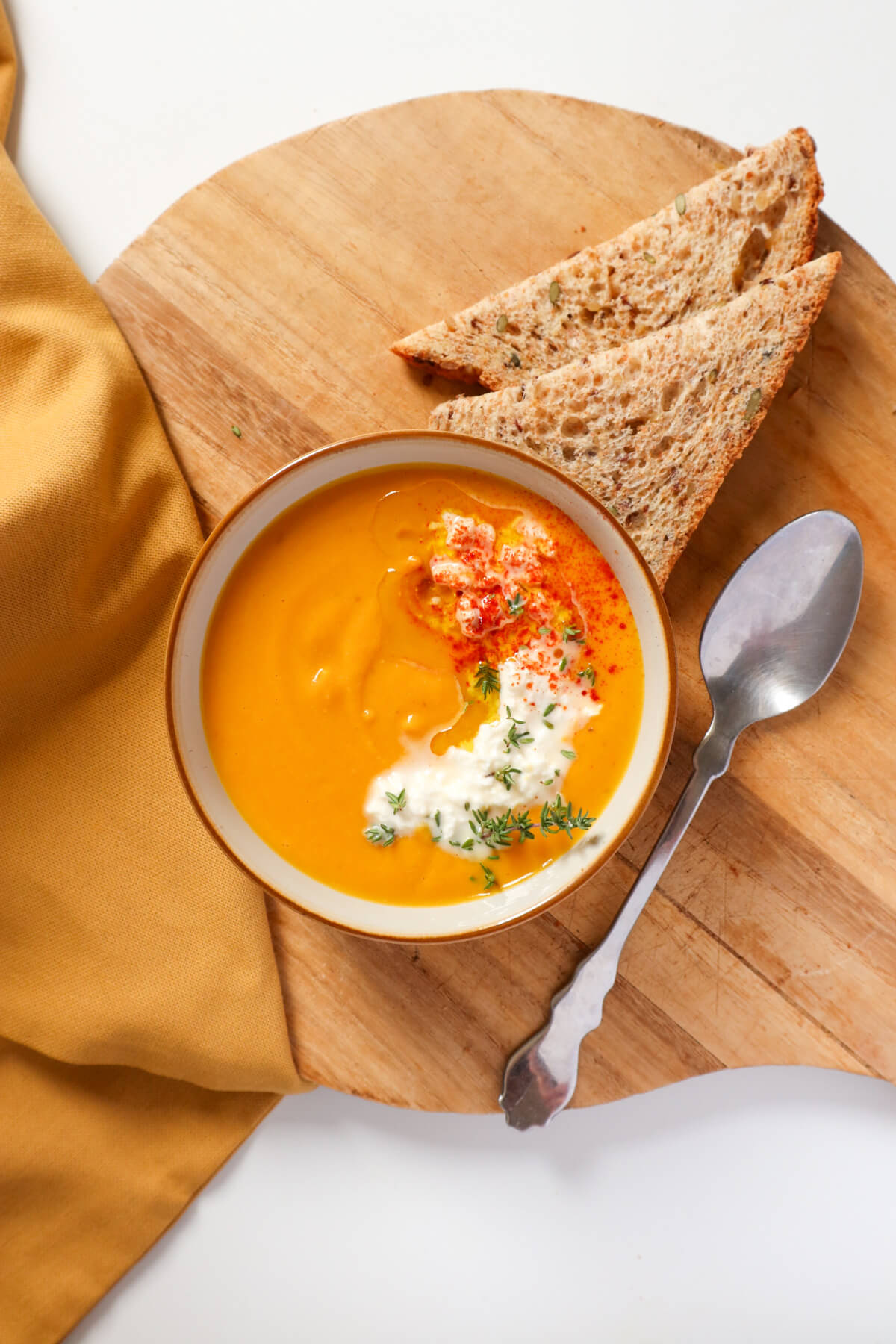 carrot and red lentil soup in a bowl topped with olive oil and feta and bread and a spoon next to it